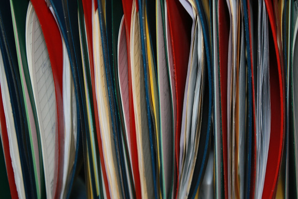 Un ensemble de documents en papier dans des classeurs de différentes couleurs, rangés à la verticale