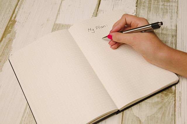 Une main avec un stylo qui prépare une écriture de plan sur un carnet de notes à petits carreaux.