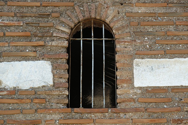 Une vieille grille en partie rouillée dans une ouverture de fenêtre sur un mur de briques et de ciment.